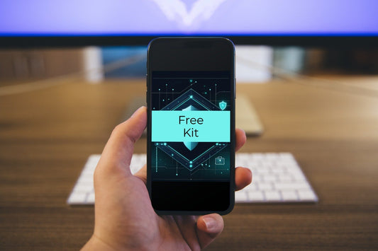 A hand holding a smartphone displaying a digital graphic with the text 'Free Kit' on a dark screen, with a blurred office desk and keyboard in the background.